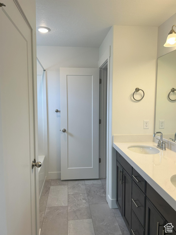 Full bath with double vanity, shower / tub combination, and baseboards