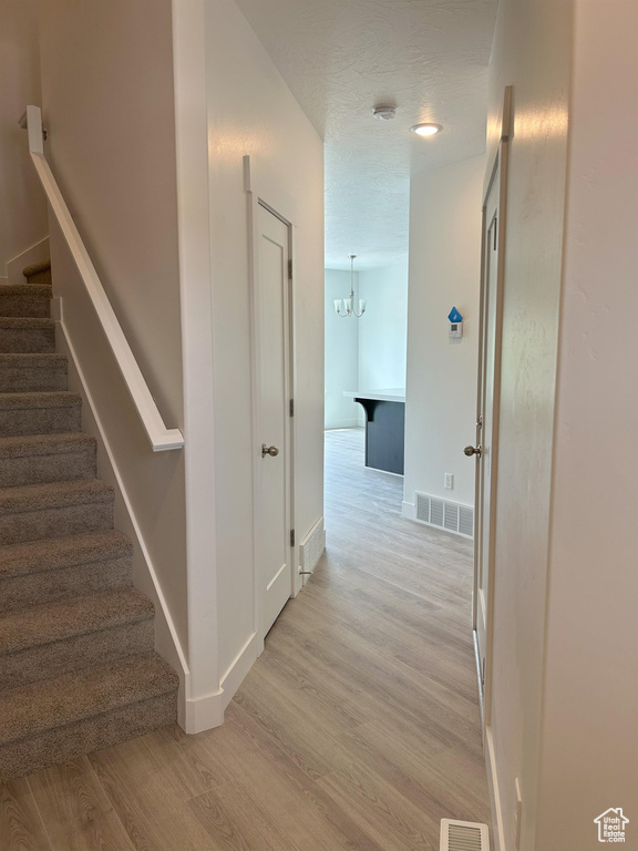 Corridor featuring stairway, light wood-style flooring, a chandelier, and baseboards