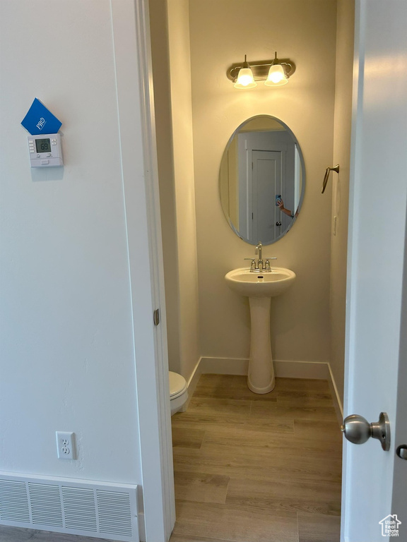 Half bathroom featuring wood finished floors, toilet, and baseboards