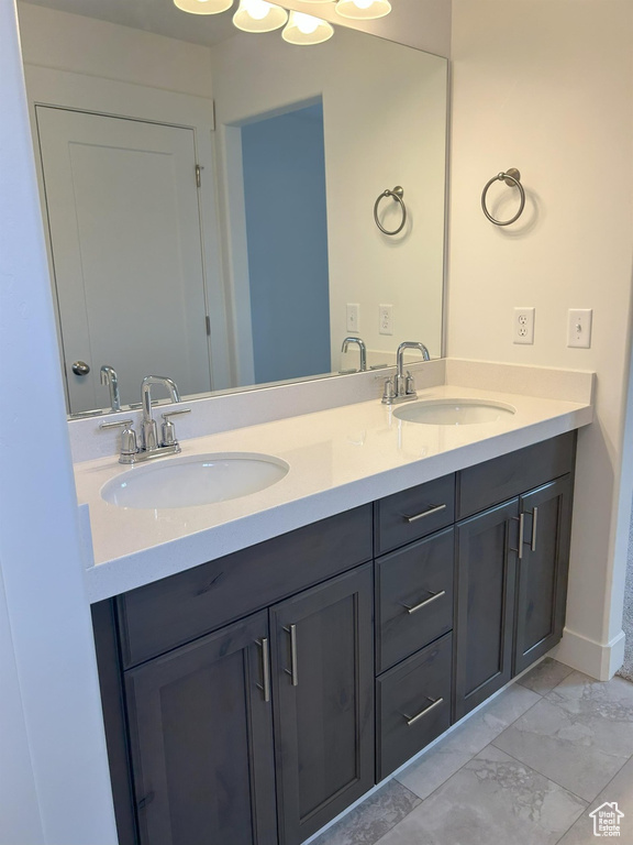 Full bath with double vanity, marble look tiles, and baseboards