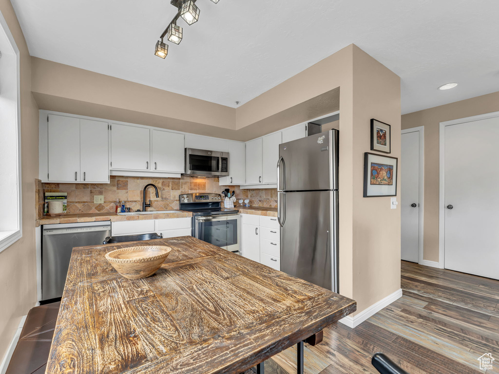 Kitchen featuring appliances with stainless steel finishes, a sink, light countertops, wood finished floors, and baseboards