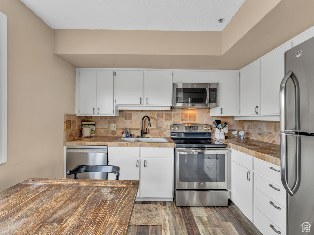 Kitchen featuring appliances with stainless steel finishes, a sink, wood finished floors, and decorative backsplash