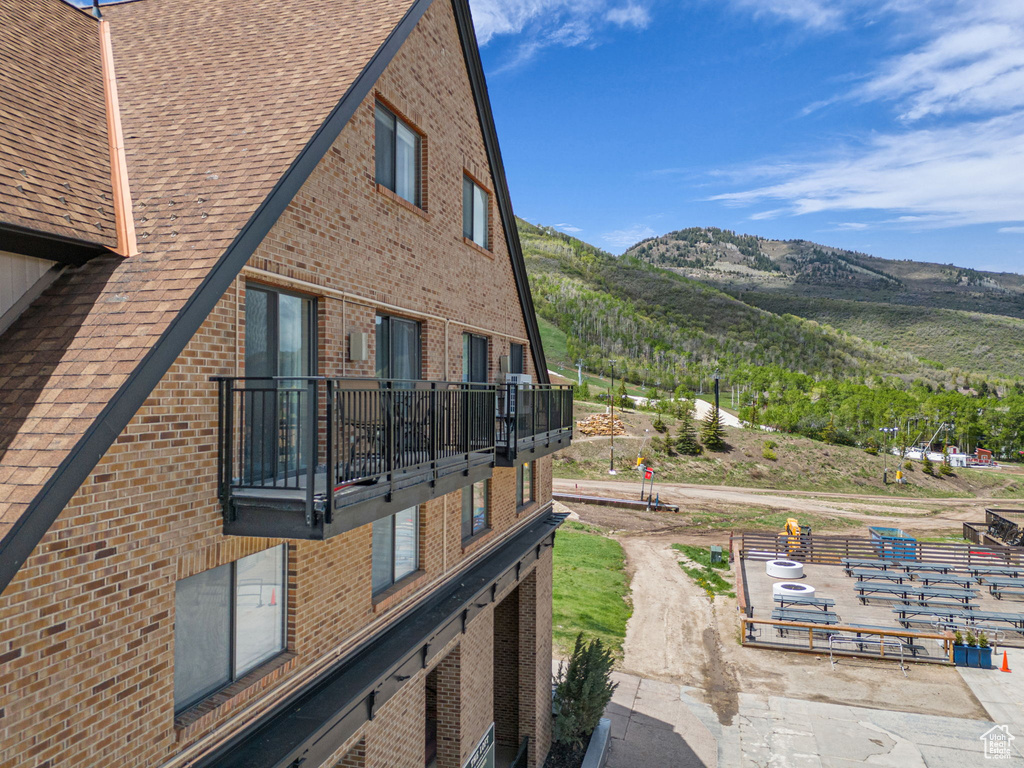 View of side of home with a balcony, brick siding, a mountain view, and a shingled roof