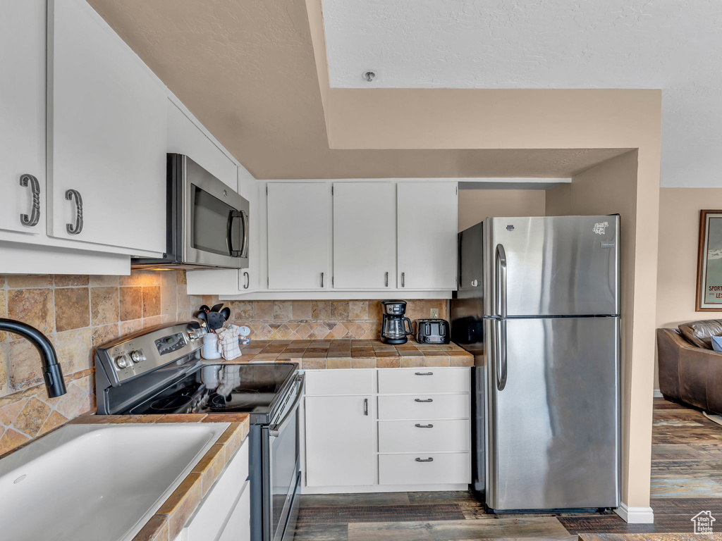 Kitchen featuring appliances with stainless steel finishes, dark wood-style flooring, a sink, and white cabinetry