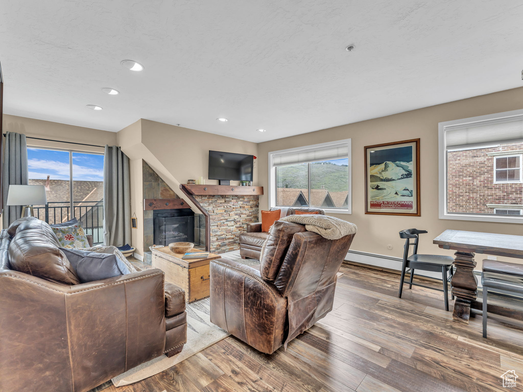 Living area with wood-type flooring, baseboards, a glass covered fireplace, a baseboard heating unit, and recessed lighting