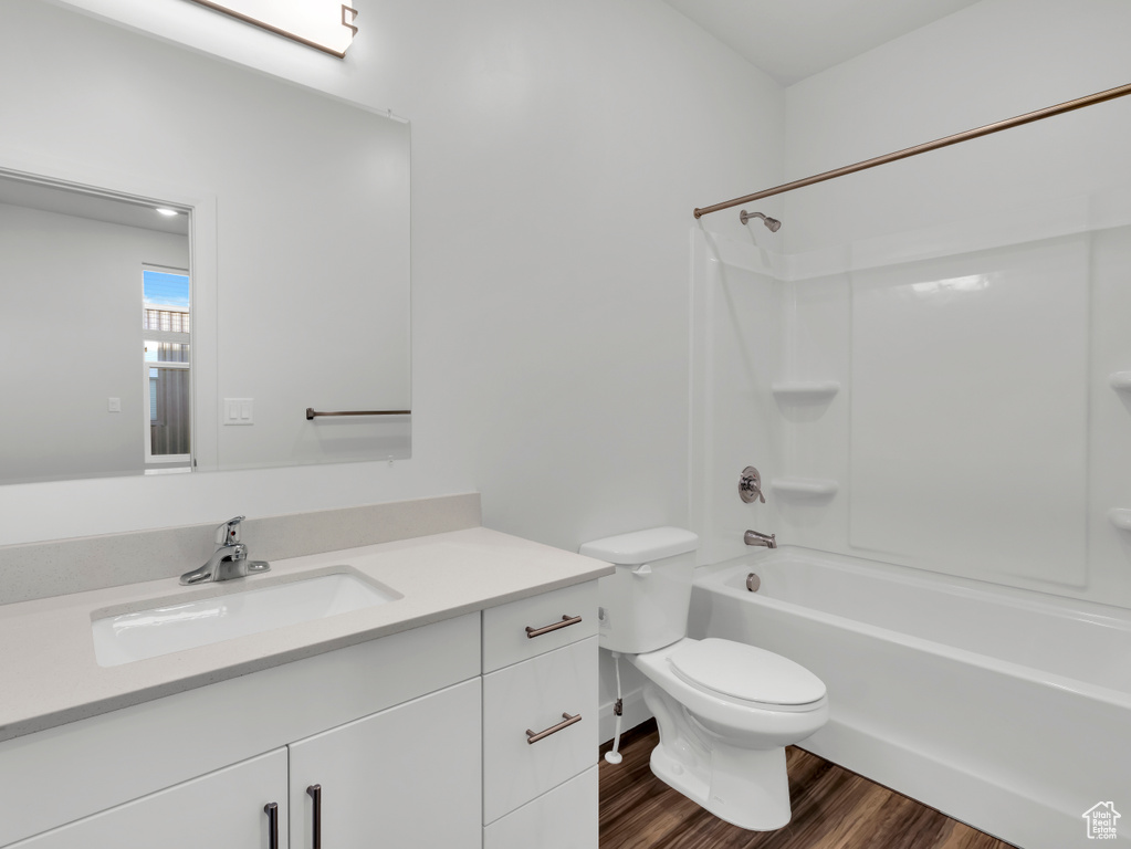Bathroom with vanity, wood finished floors, toilet, and washtub / shower combination