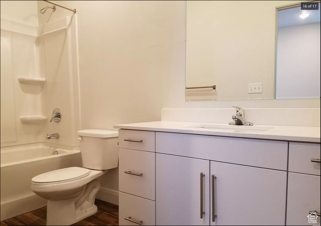 Bathroom with vanity, toilet, shower / tub combination, wood finished floors, and baseboards