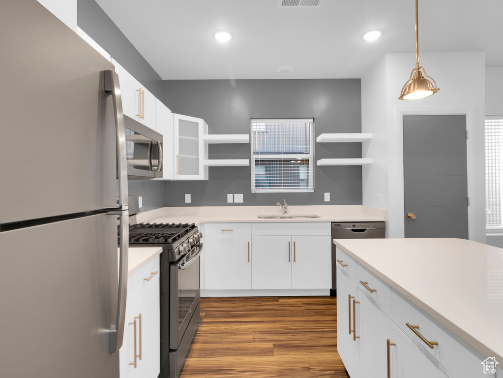 Kitchen with appliances with stainless steel finishes, open shelves, a sink, wood finished floors, and white cabinets