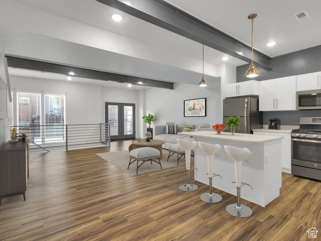 Kitchen featuring stainless steel appliances, open floor plan, white cabinets, a breakfast bar, and dark wood-type flooring