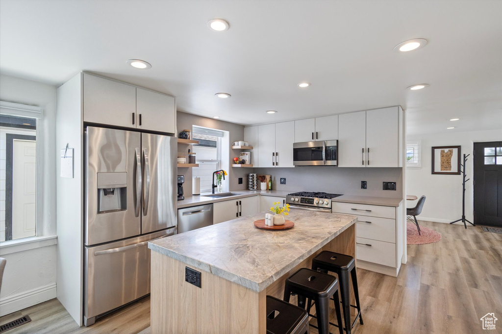 Kitchen featuring appliances with stainless steel finishes, light countertops, a sink, open shelves, and light wood-type flooring
