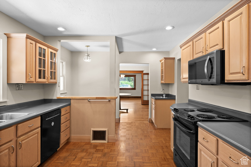 Kitchen featuring black appliances, dark countertops, a sink, light brown cabinetry, and recessed lighting