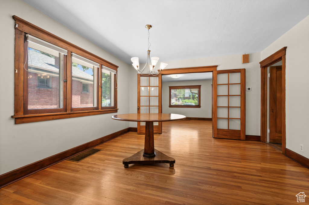 Unfurnished dining area with a chandelier, plenty of natural light, baseboards, and wood finished floors