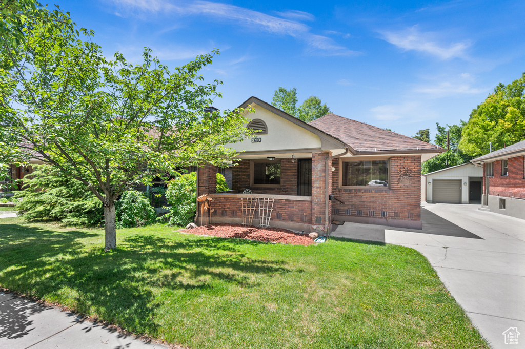View of front of property featuring an outbuilding, brick siding, concrete driveway, a front yard, and a detached garage