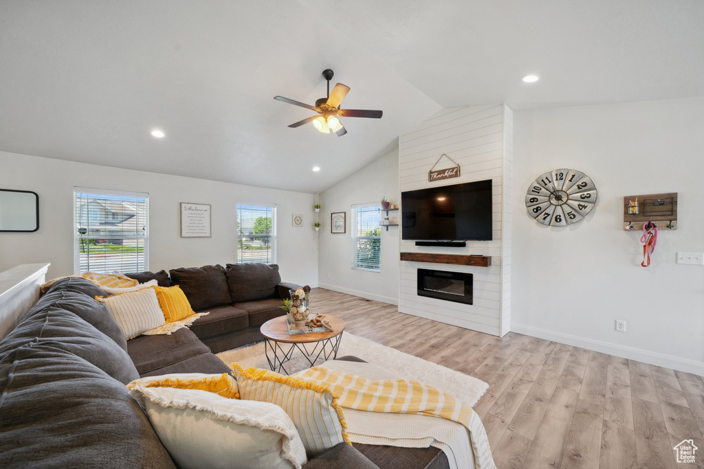 Living area with a ceiling fan, plenty of natural light, light wood-style flooring, a fireplace, and vaulted ceiling