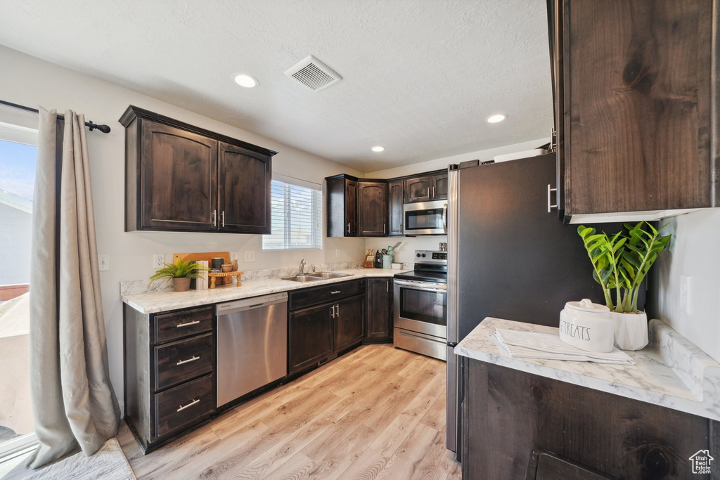Kitchen featuring stainless steel appliances, a sink, dark brown cabinets, light wood finished floors, and light countertops