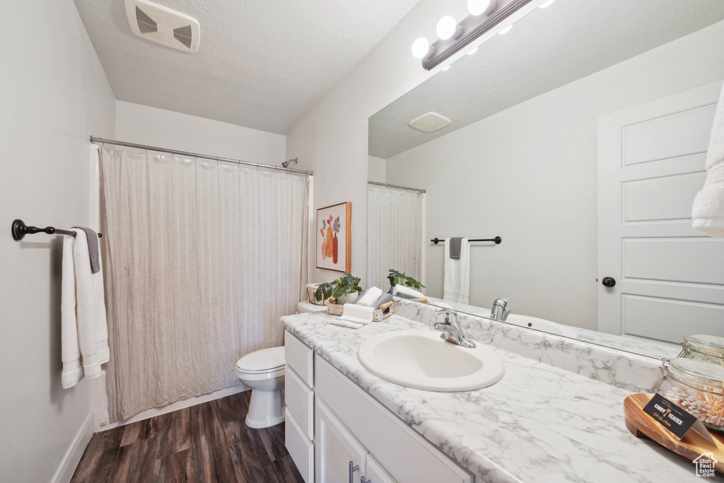 Full bathroom with vanity, toilet, wood finished floors, baseboards, and a shower with curtain