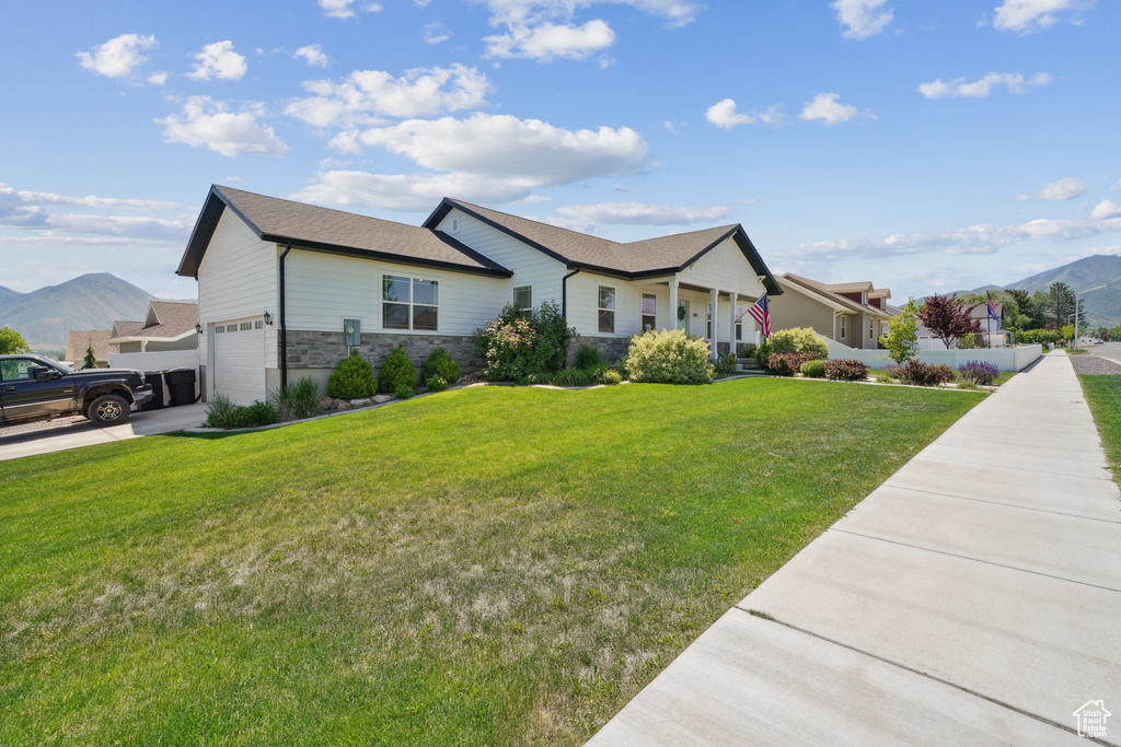 Ranch-style house featuring stone siding, a garage, a front yard, and a mountain view