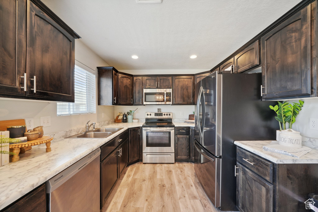 Kitchen featuring stainless steel appliances, a sink, light wood-style floors, dark brown cabinets, and recessed lighting