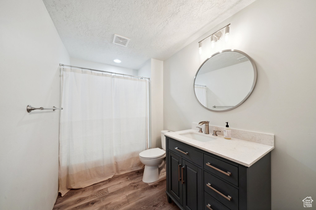 Full bath with a textured ceiling, wood finished floors, vanity, and toilet