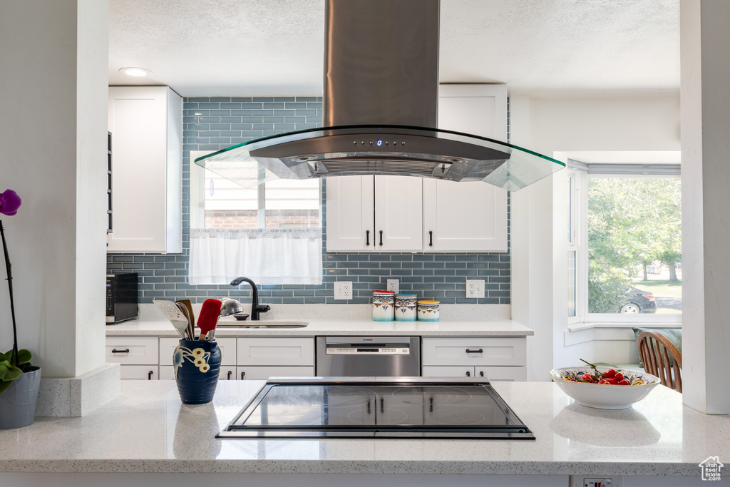 Kitchen featuring stainless steel dishwasher, a sink, island range hood, white cabinetry, and a textured ceiling