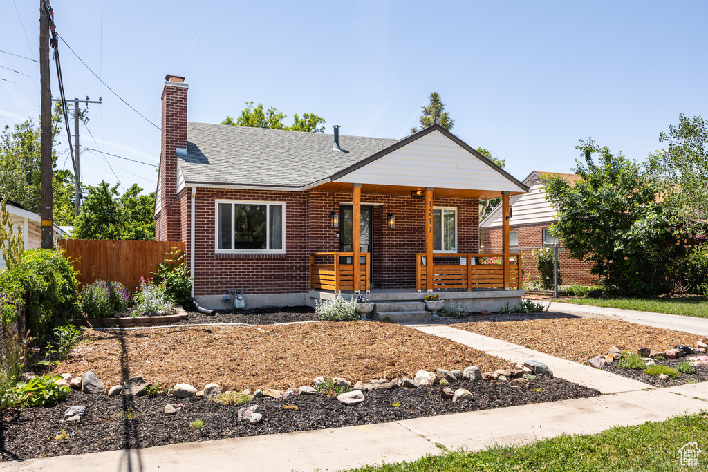 View of front facade featuring covered porch, brick siding, a chimney, and roof with shingles