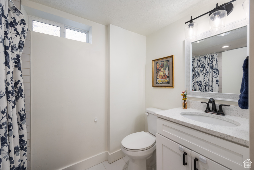 Full bath featuring toilet, vanity, tile patterned floors, baseboards, and a textured ceiling