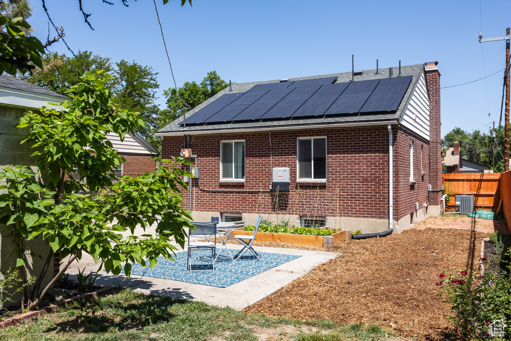 Back of property with central AC, roof mounted solar panels, a chimney, brick siding, and a patio area