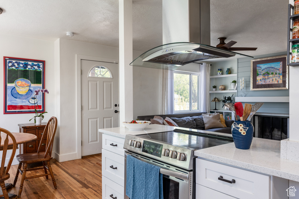 Kitchen featuring stainless steel range with electric cooktop, island exhaust hood, light wood-style floors, light stone countertops, and healthy amount of natural light