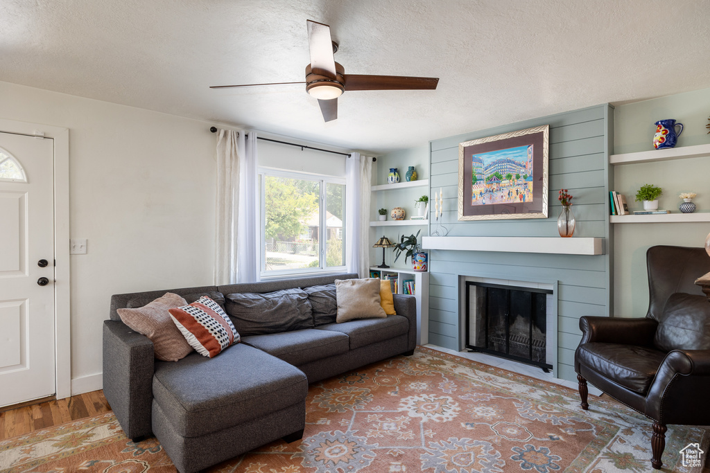 Living area featuring a ceiling fan, wood finished floors, a large fireplace, and a textured ceiling
