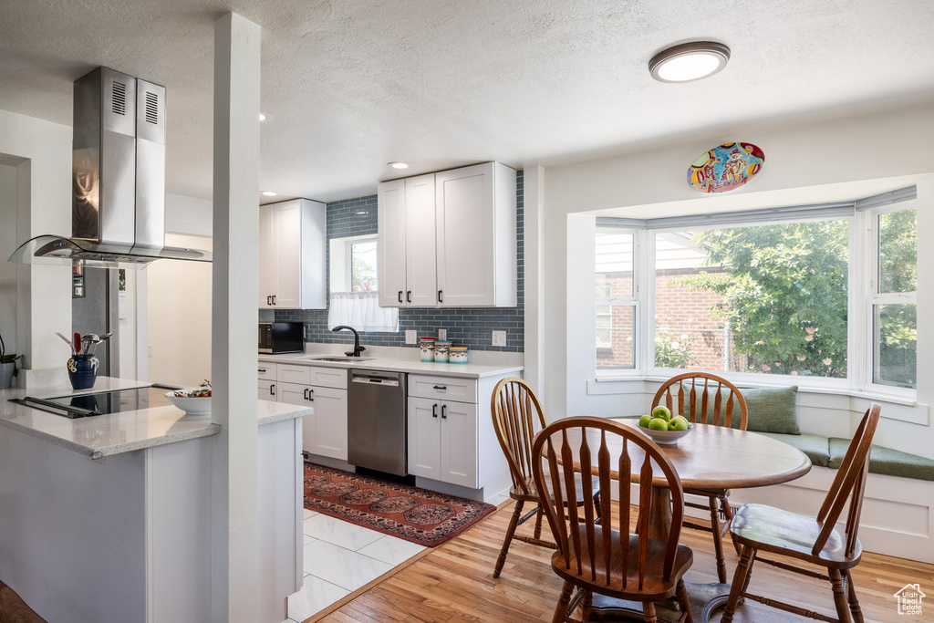 Kitchen featuring dishwasher, island range hood, tasteful backsplash, a sink, and white cabinets