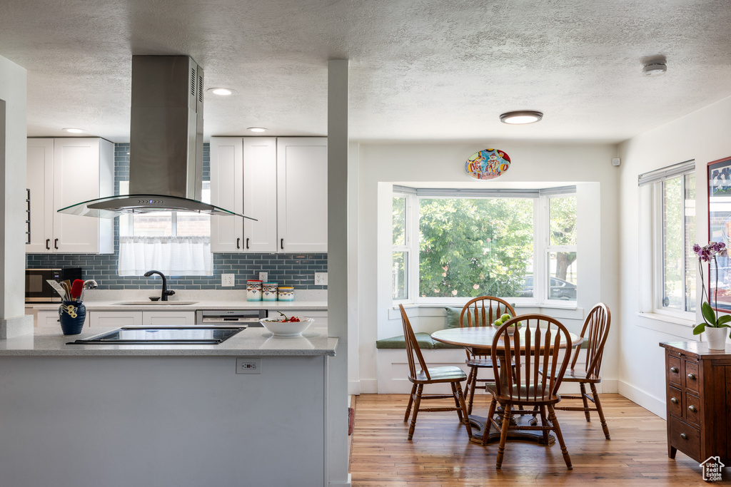 Kitchen with island exhaust hood, light wood-type flooring, a sink, decorative backsplash, and white cabinetry