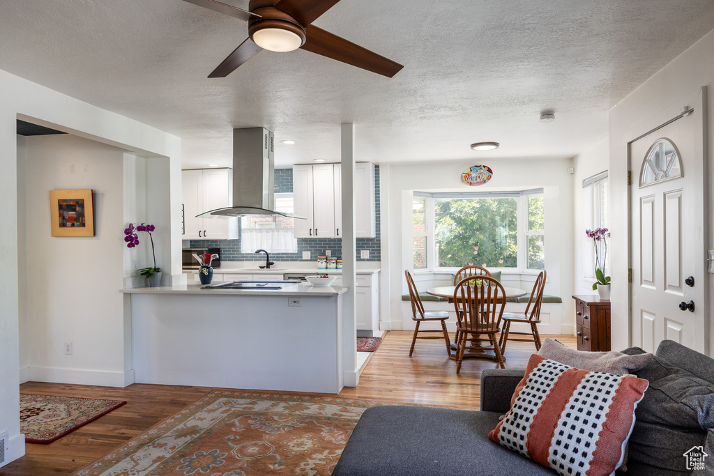 Kitchen with island exhaust hood, white cabinets, ceiling fan, backsplash, and light wood-style flooring