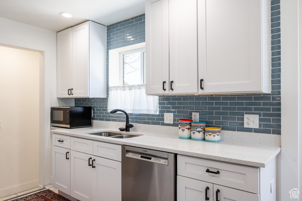 Kitchen with dishwasher, a sink, black microwave, and white cabinets