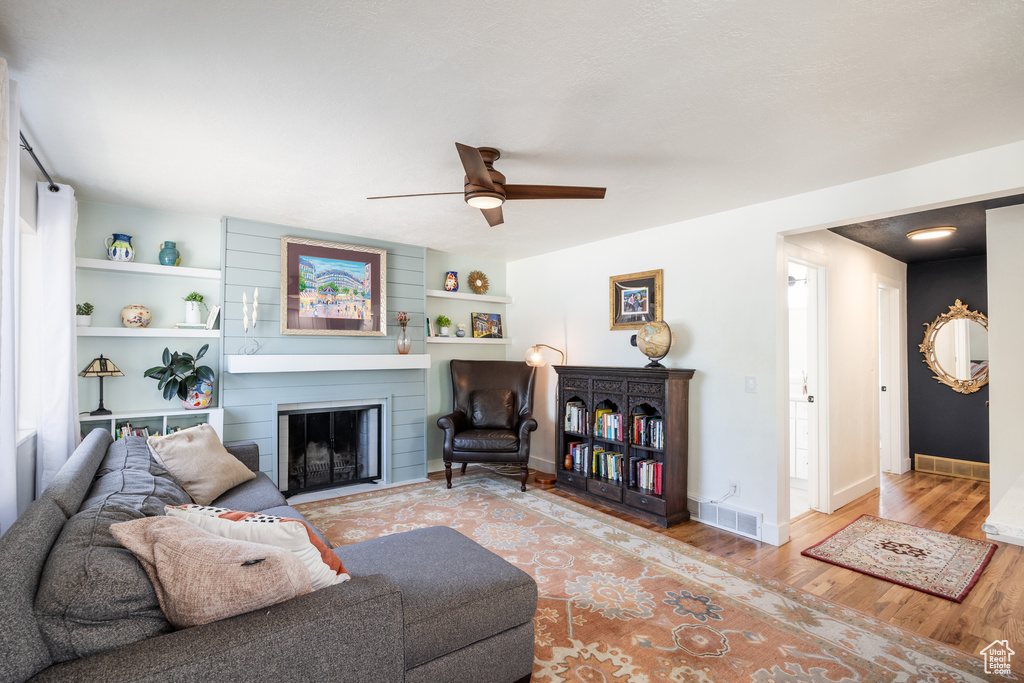 Living area featuring wood finished floors, a fireplace, ceiling fan, and built in features