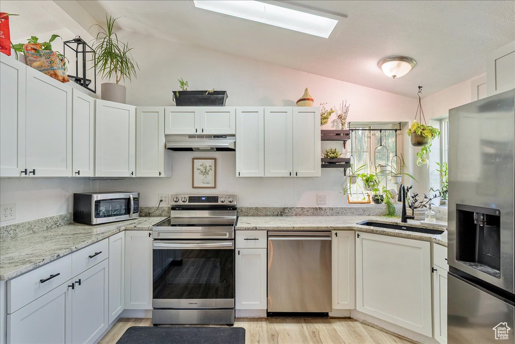Kitchen featuring stainless steel appliances, under cabinet range hood, a sink, lofted ceiling, and open shelves