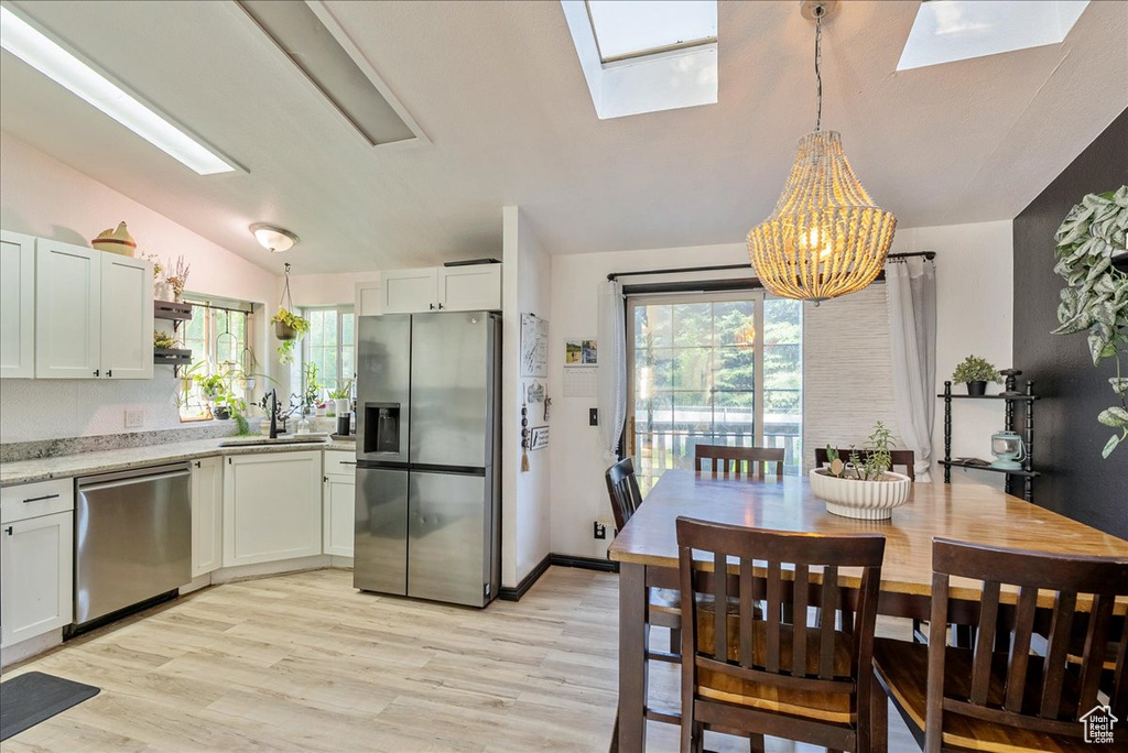Dining area with a skylight, vaulted ceiling, a chandelier, and light wood finished floors