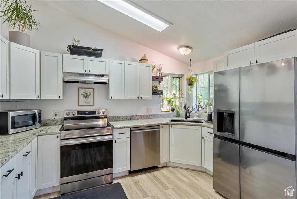 Kitchen with stainless steel appliances, under cabinet range hood, lofted ceiling, a sink, and light wood-style floors