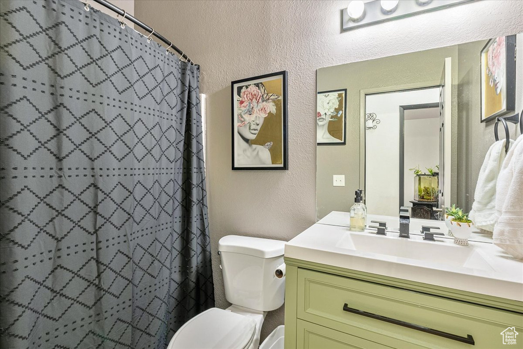 Bathroom with a textured wall, toilet, vanity, and curtained shower