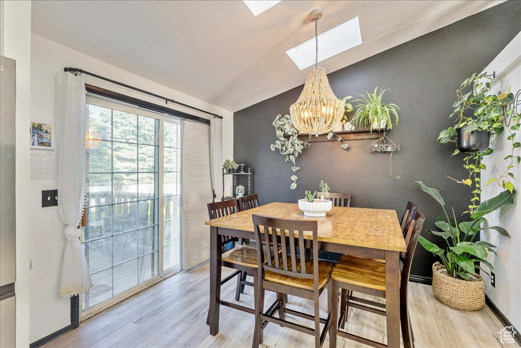 Dining area featuring wood finished floors, a skylight, lofted ceiling, a chandelier, and baseboards