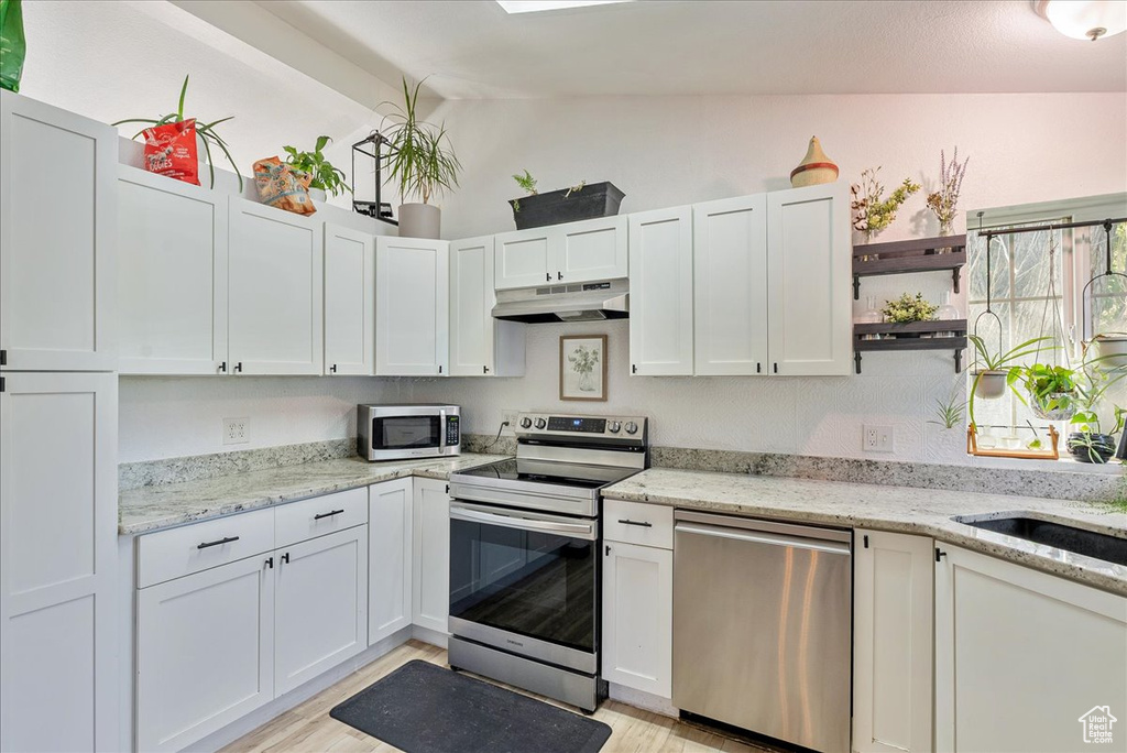 Kitchen with stainless steel appliances, under cabinet range hood, vaulted ceiling, open shelves, and light wood-style flooring