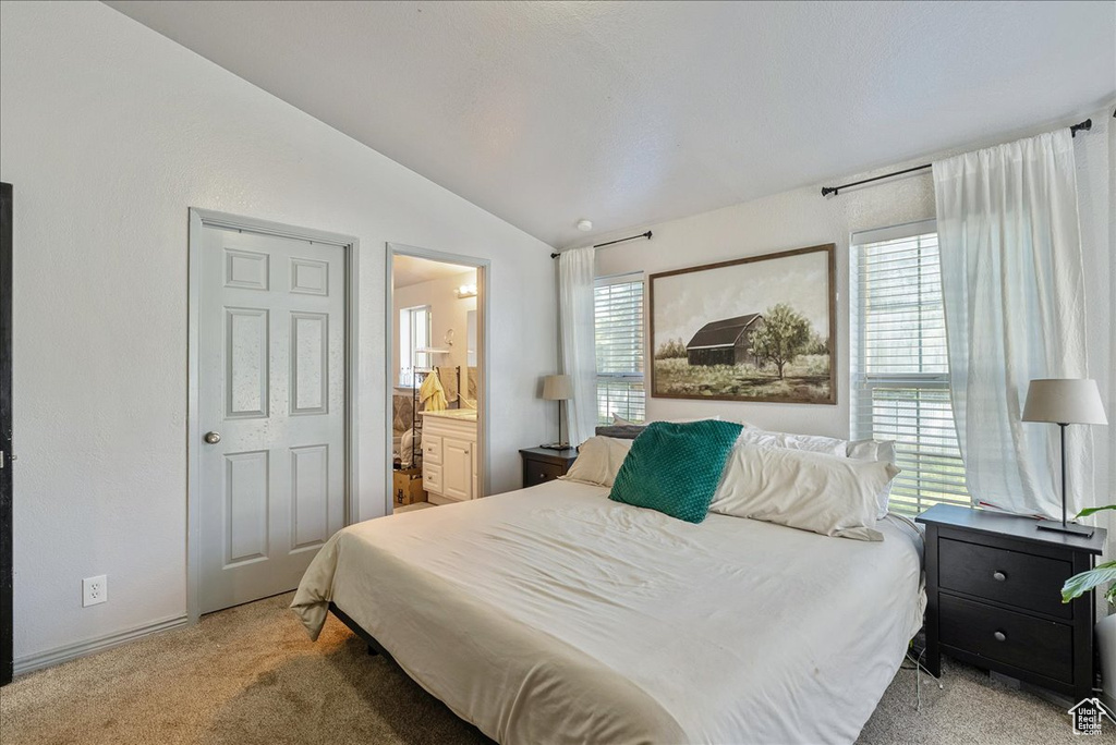Bedroom with lofted ceiling, light carpet, and ensuite bathroom