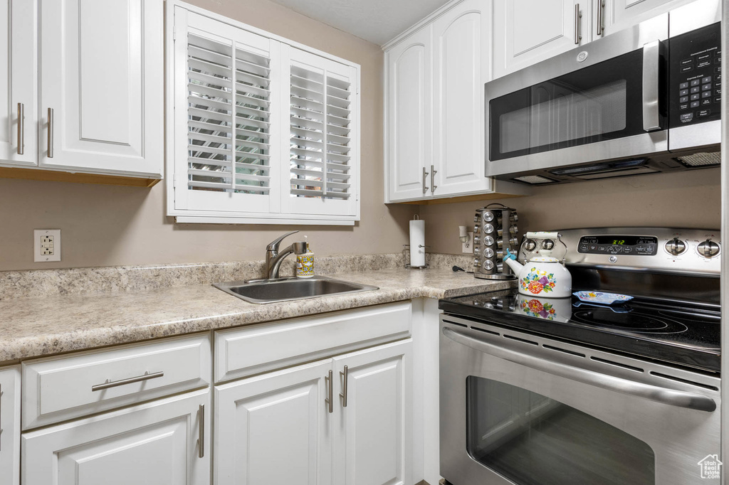 Kitchen featuring appliances with stainless steel finishes, a sink, white cabinetry, and light countertops