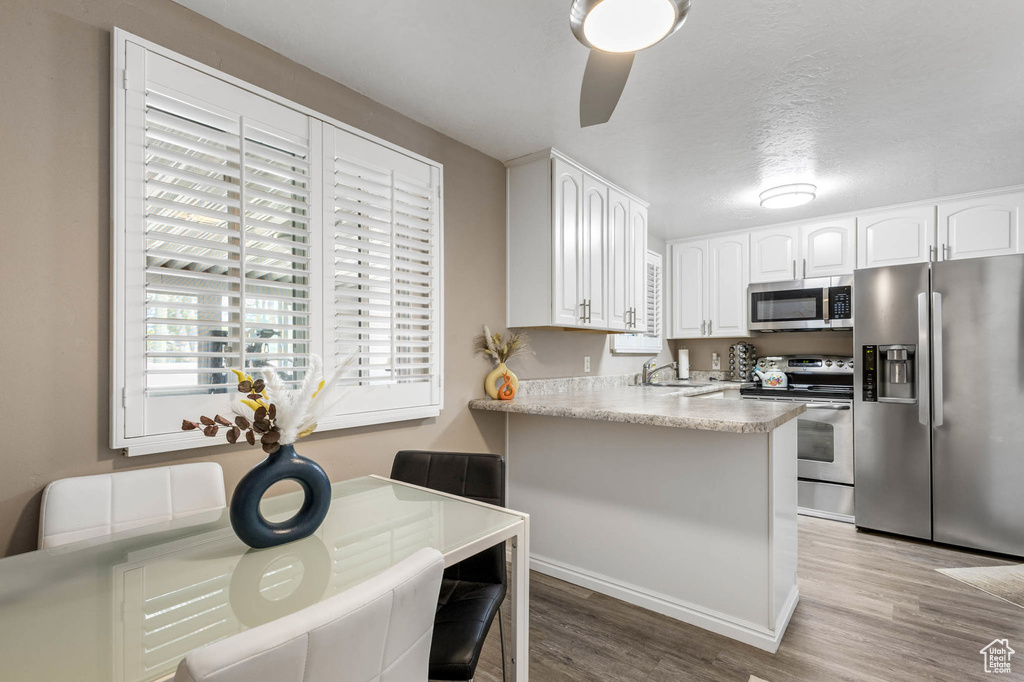 Kitchen with appliances with stainless steel finishes, light wood-style flooring, white cabinets, a peninsula, and ceiling fan