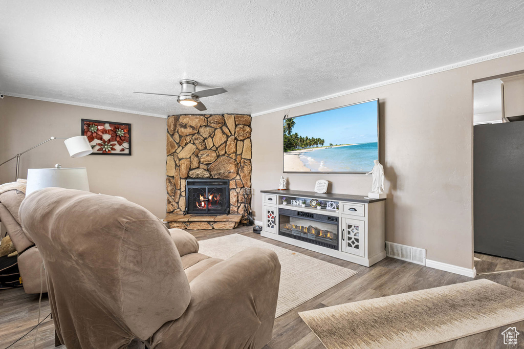 Living area featuring ceiling fan, ornamental molding, baseboards, wood finished floors, and a stone fireplace
