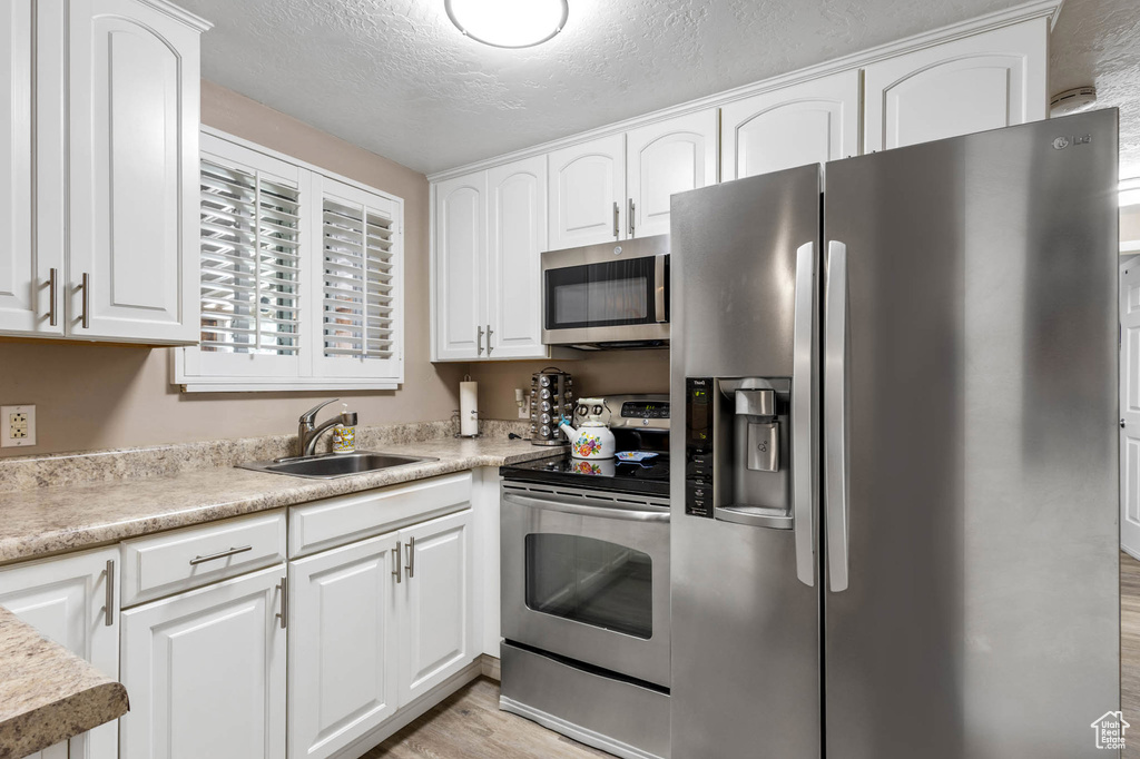 Kitchen with stainless steel appliances, light wood-style floors, a sink, white cabinetry, and light countertops