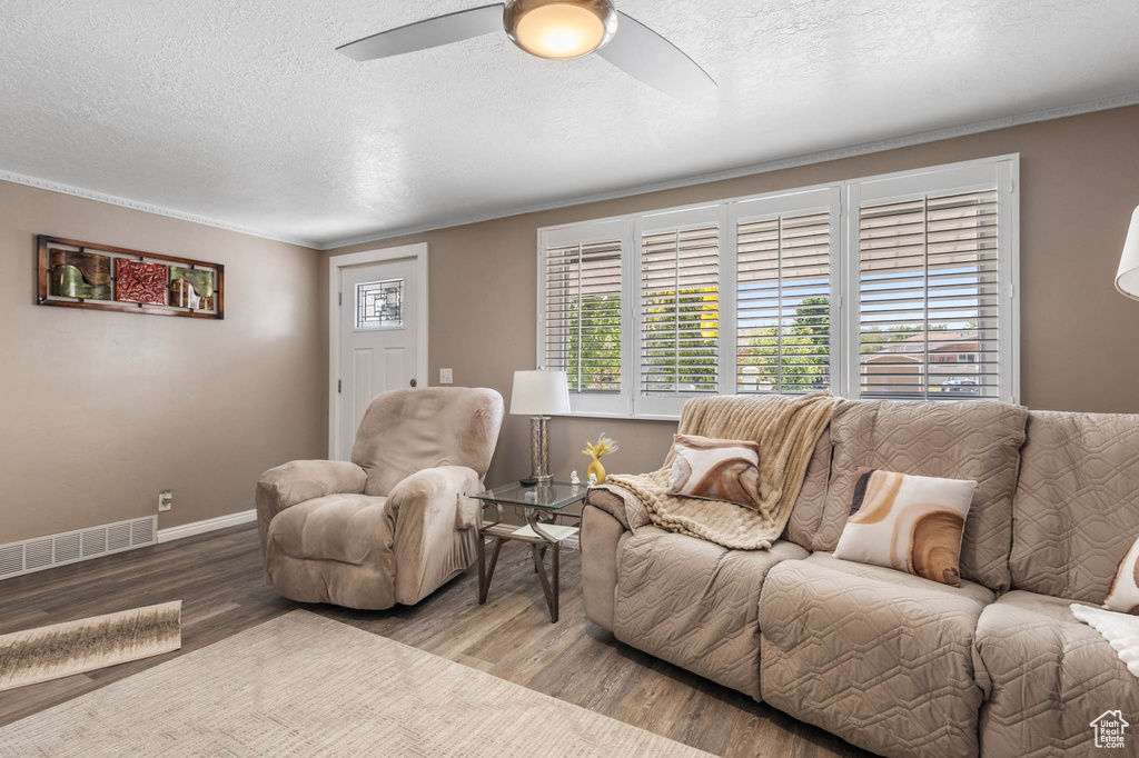 Living room featuring wood finished floors, a textured ceiling, a ceiling fan, baseboards, and ornamental molding