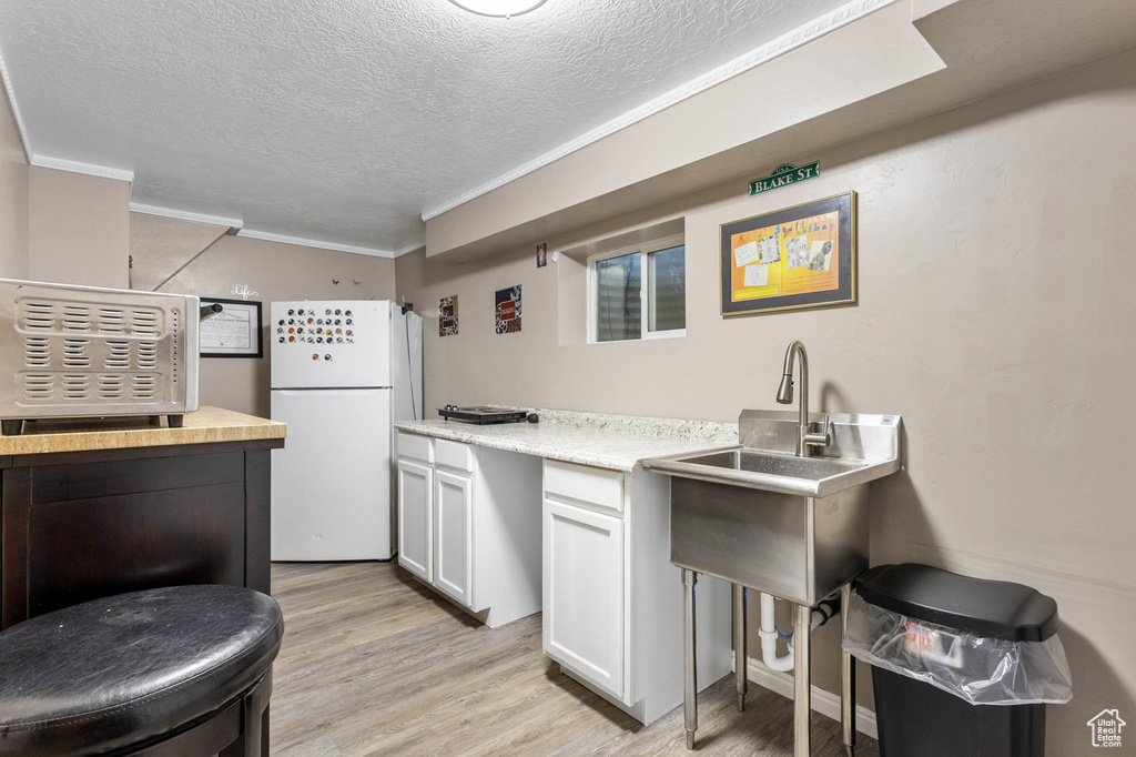 Kitchen featuring freestanding refrigerator, light wood-type flooring, a textured ceiling, crown molding, and light countertops