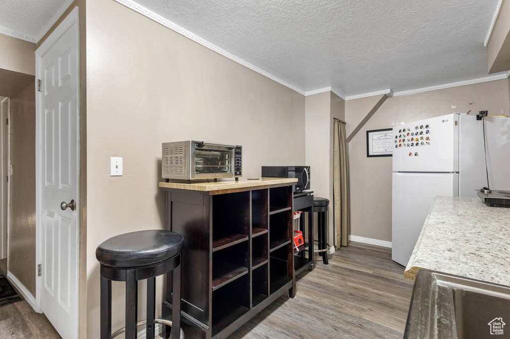 Kitchen with freestanding refrigerator, wood finished floors, a textured ceiling, crown molding, and baseboards