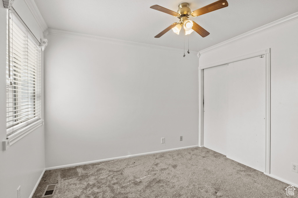 Unfurnished bedroom with ornamental molding, carpet, a closet, baseboards, and a ceiling fan