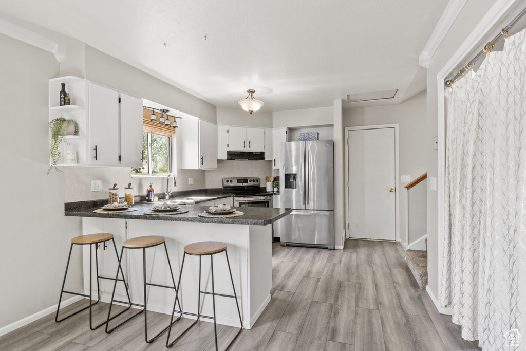 Kitchen featuring appliances with stainless steel finishes, open shelves, under cabinet range hood, dark countertops, and a peninsula